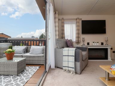 A living room with a gray armchair next to a fireplace and a wall-mounted TV at Lodge 36 - Kingfisher Lodge in Wickhamford near Evesham
