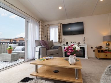 A living room with a gray armchair wooden coffee table with flowers and magazines and a wall-mounted TV at Lodge 36 - Kingfisher Lodge in Wickhamford near Evesham