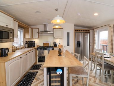A kitchen with wooden countertops a kitchen island with a bottle and wine glasses stainless steel appliances and a dining table at Lodge 36 - Kingfisher Lodge in Wickhamford near Evesham