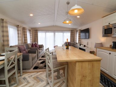 A living room and kitchen area with a wooden table island chairs sofas and windows with curtains at Lodge 36 - Kingfisher Lodge in Wickhamford near Evesham