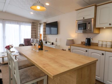 A kitchen area with wooden countertop a bottle and glasses on the table a microwave kettle and canisters on the counter at Lodge 36 - Kingfisher Lodge in Wickhamford near Evesham