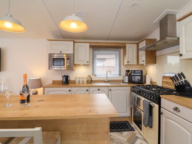 A kitchen with wooden countertops a gas stove a microwave and a window with blinds at Lodge 36 - Kingfisher Lodge in Wickhamford near Evesham