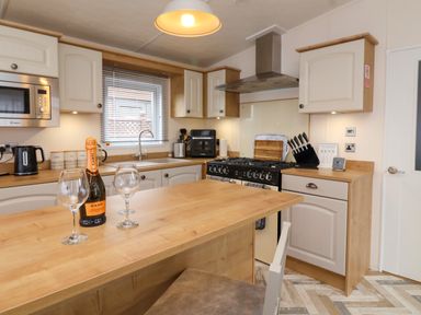 A kitchen with a wooden island countertop two wine glasses and a bottle of prosecco at Lodge 36 - Kingfisher Lodge in Wickhamford near Evesham