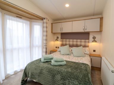 A bedroom with a bed folded towels on the bed next to windows at Lodge 36 - Kingfisher Lodge in Wickhamford near Evesham