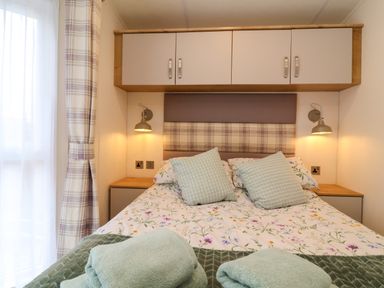A bedroom with a double bed two pillows wall lamps and overhead storage cabinets at Lodge 36 - Kingfisher Lodge in Wickhamford near Evesham