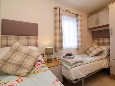 A bedroom with two single beds a lamp on a bedside table and a window with curtains at Lodge 36 - Kingfisher Lodge in Wickhamford near Evesham