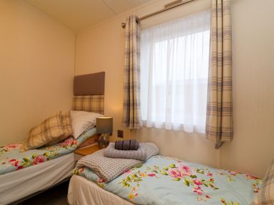 A bedroom with two single beds with floral bedding and plaid cushions and curtains at Lodge 36 - Kingfisher Lodge in Wickhamford near Evesham