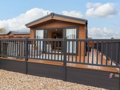 A wooden lodge with a deck and railings at Lodge 36 - Kingfisher Lodge in Wickhamford near Evesham