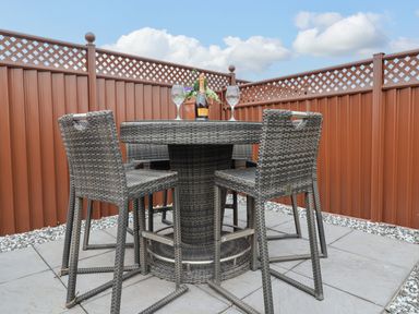 An outdoor patio area with a round table and four woven chairs a bottle and two glasses on the table at Lodge 36 - Kingfisher Lodge in Wickhamford near Evesham
