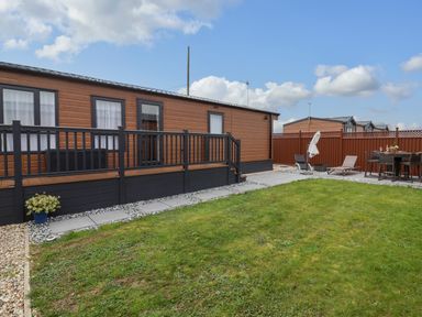 A garden with lawn chairs and dining table next to a brown wooden lodge at Lodge 36 - Kingfisher Lodge in Wickhamford near Evesham