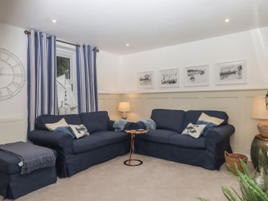A living room with two navy blue sofas a small round table between them striped curtains and framed pictures on the wall at Pie Cottage in Teignmouth