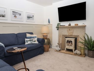 A living room with blue sofas a small metal side table a lamp on a round side table and a fireplace with decorations at Pie Cottage in Teignmouth