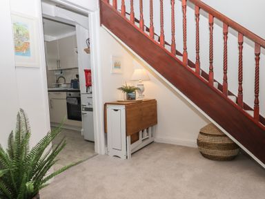An area under a staircase with a small table lamp on a folding table and a basket next to it at Pie Cottage in Teignmouth