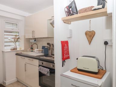 A compact kitchen with white cabinets a sink stove oven a kettle and toaster on a shelf at Pie Cottage in Teignmouth