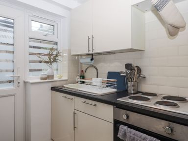 A kitchen counter with sink dish rack electric stove and cooking utensils at Pie Cottage in Teignmouth
