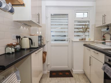 A kitchen with black countertops white cabinets and a back door with frosted glass at Pie Cottage in Teignmouth