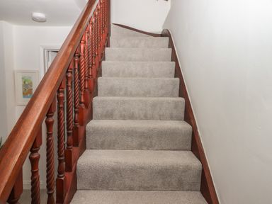 Carpeted stairs with wooden banister and white walls at Pie Cottage in Teignmouth