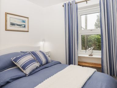 A bedroom with a bed covered in blue bedding and striped pillows next to a window with matching blue and white striped curtains at Pie Cottage in Teignmouth