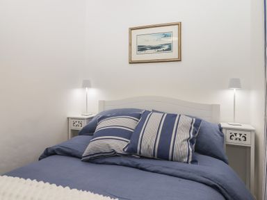 A bedroom with a bed blue bedding two nightstands with lamps and a framed picture at Pie Cottage in Teignmouth