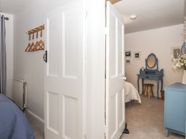 A room with a partially open white door wooden coat hooks with hangers a blue dressing table with mirror a wooden stool and a blue cabinet at Pie Cottage in Teignmouth