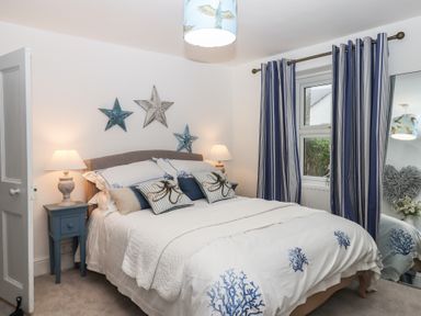 A bedroom with a double bed with coral patterned bedding and star wall decorations at Pie Cottage in Teignmouth