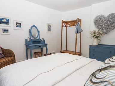 A bedroom with a bed a blue dressing table a wooden clothes rack and a chest of drawers with flowers at Pie Cottage in Teignmouth