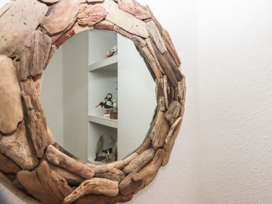 A round mirror with a driftwood frame reflecting shelves with bird figurines at Pie Cottage in Teignmouth