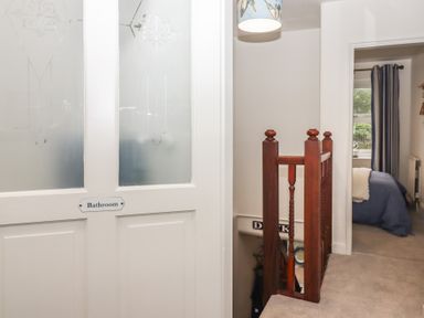 A hallway with a bathroom door and wooden railing next to a bedroom at Pie Cottage in Teignmouth