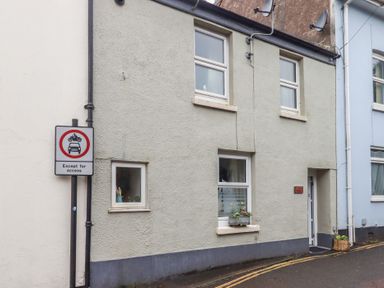 The exterior of a building with three windows a door a traffic sign and flower pots on the window ledge and ground at Pie Cottage in Teignmouth