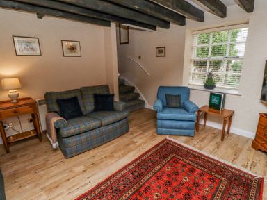 A living room with a sofa and armchair a red patterned rug wooden side tables and a window at Timberwick Green in Akeld near Wooler