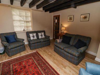 A living room with plaid sofas and armchairs a red rug and a side table with a lamp at Timberwick Green Akeld near Wooler