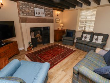 A living room with a fireplace armchairs sofas a wooden cabinet and a television at Timberwick Green in Akeld near Wooler