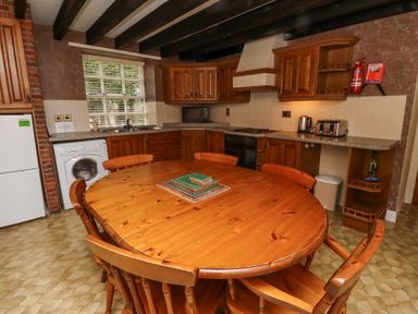A kitchen with wooden cabinets a round wooden table and chairs a washing machine and appliances at Timberwick Green in Akeld near Wooler