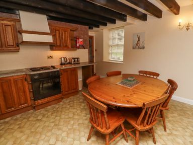 A kitchen with wooden cabinets a round wooden dining table with chairs and kitchen appliances at Timberwick Green in Akeld near Wooler