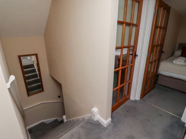 A carpeted staircase with beige walls and a mirror on the wall next to two wooden framed glass doors leading to bedrooms at Timberwick Green Akeld near Wooler