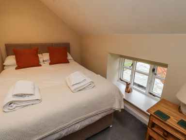 A bedroom with a bed with white bedding and two orange pillows a window with a small decorative figurine and a wooden nightstand with a lamp at Timberwick Green Akeld near Wooler