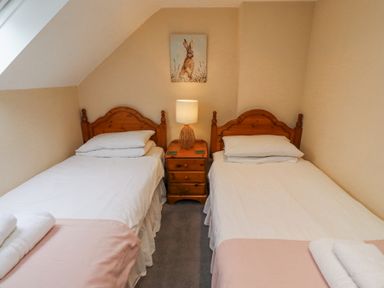 A bedroom with two single beds wooden headboards bedside table with lamp and a painting at Timberwick Green in Akeld near Wooler
