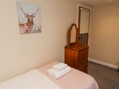 A bedroom with a bed with folded towels on it a wooden dresser with a mirror a door with a roller blind and a painting of a stag on the wall at Timberwick Green Akeld near Wooler