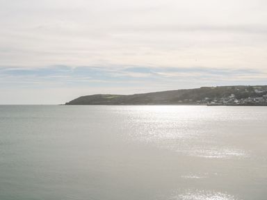 A coastal landscape with a calm sea and a headland with buildings and greenery at Sea View Loft in Rosudgeon