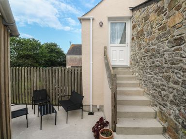 An outdoor patio area with black metal chairs and table next to stone and plaster walls with steps leading to a white door at Sea View Loft in Rosudgeon