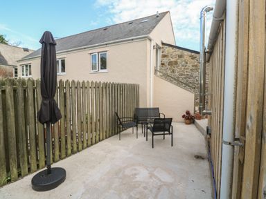 An outdoor patio area with black metal chairs and a closed black umbrella next to a wooden fence at Sea View Loft in Rosudgeon