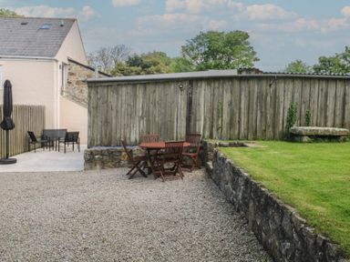 An outdoor area with gravel ground and wooden table with chairs next to a stone wall and a grass lawn at Sea View Loft in Rosudgeon
