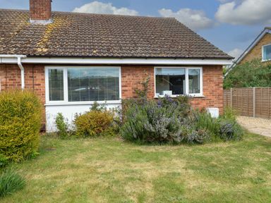 A brick house with two windows and bushes in front with a grassy lawn at Little Lodge in Dersingham