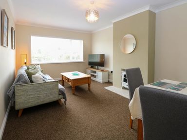 A living room with a sofa a coffee table a TV on a stand a round mirror on the wall and dining chairs at Little Lodge in Dersingham