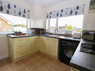 A kitchen with wooden cabinets a washing machine a sink a toaster a microwave a kettle and cups on the counter at Little Lodge in Dersingham