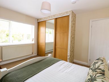 A bedroom with a bed a green blanket a window with blinds a radiator and a mirrored wardrobe at Little Lodge in Dersingham