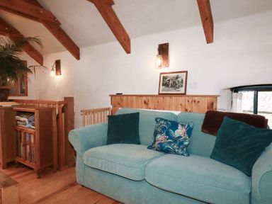 A snug room with a teal sofa and wooden features at Stribleys Barn in Cusgarne near St Day