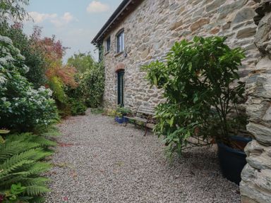 A garden with a stone wall and gravel pathway at Stribleys Barn Cusgarne near St Day
