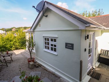 A small exterior side view of a light green building with a window a door a satellite dish and a sign that says Little Acorns with outdoor seating and plants at Little Acorns in Gweek