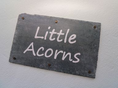 A rectangular stone plaque with the text Little Acorns mounted on a white wall at Little Acorns in Gweek
